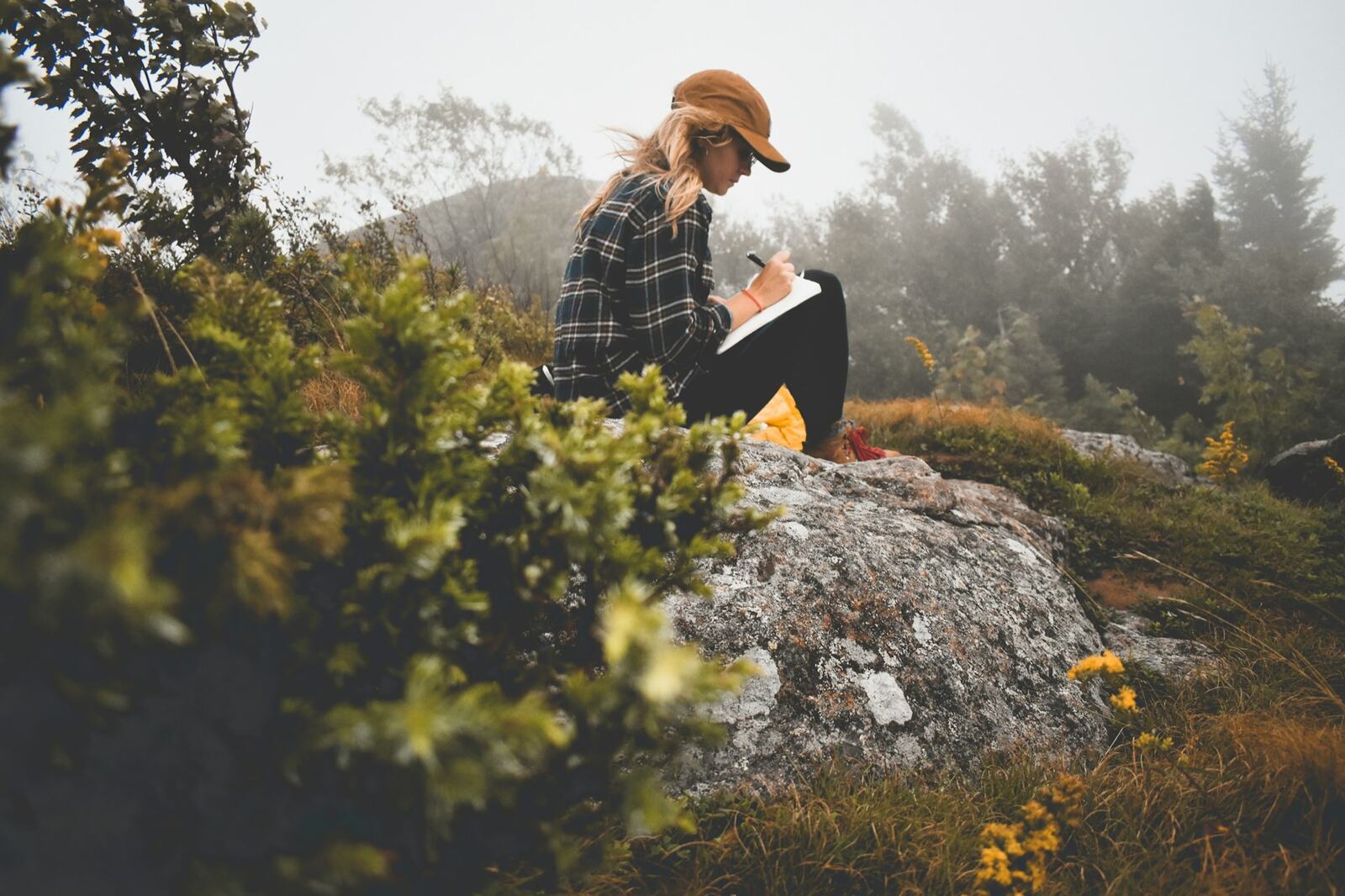 A woman sitting on a rock outdoors, writing in a notebook